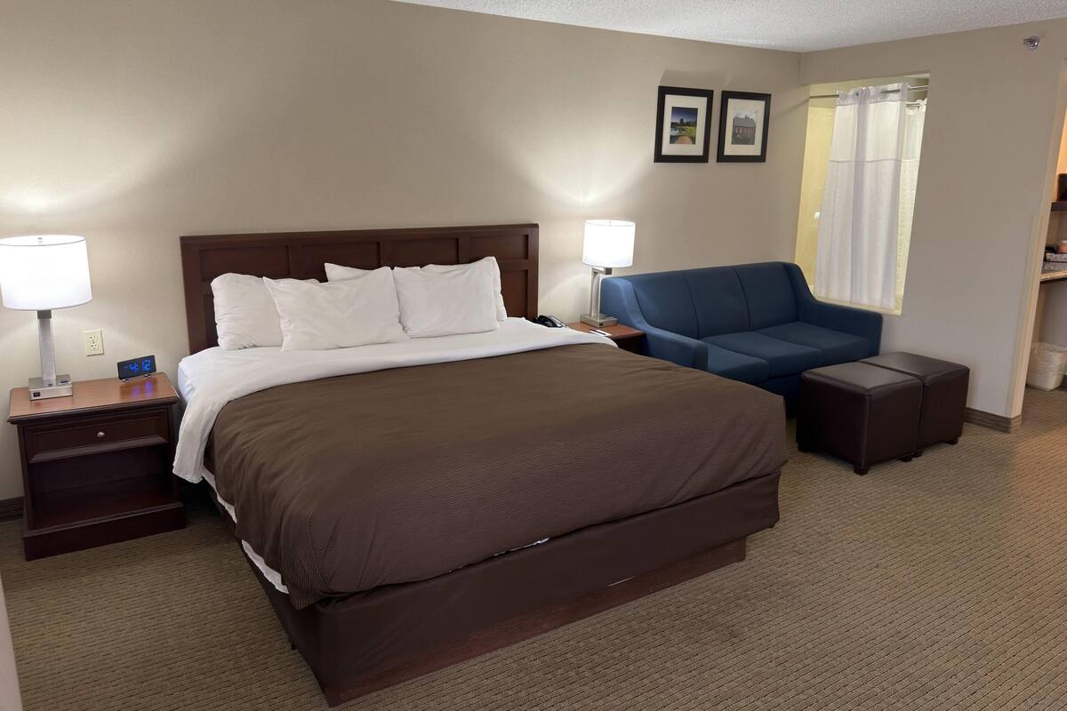 A hotel room with a large bed, two bedside tables, a desk, a chair, and a window with curtains.