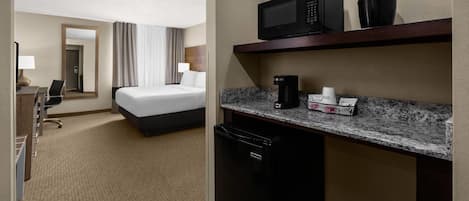 A hotel room with a bed, a desk, a microwave, a coffee maker, and a trash bin.