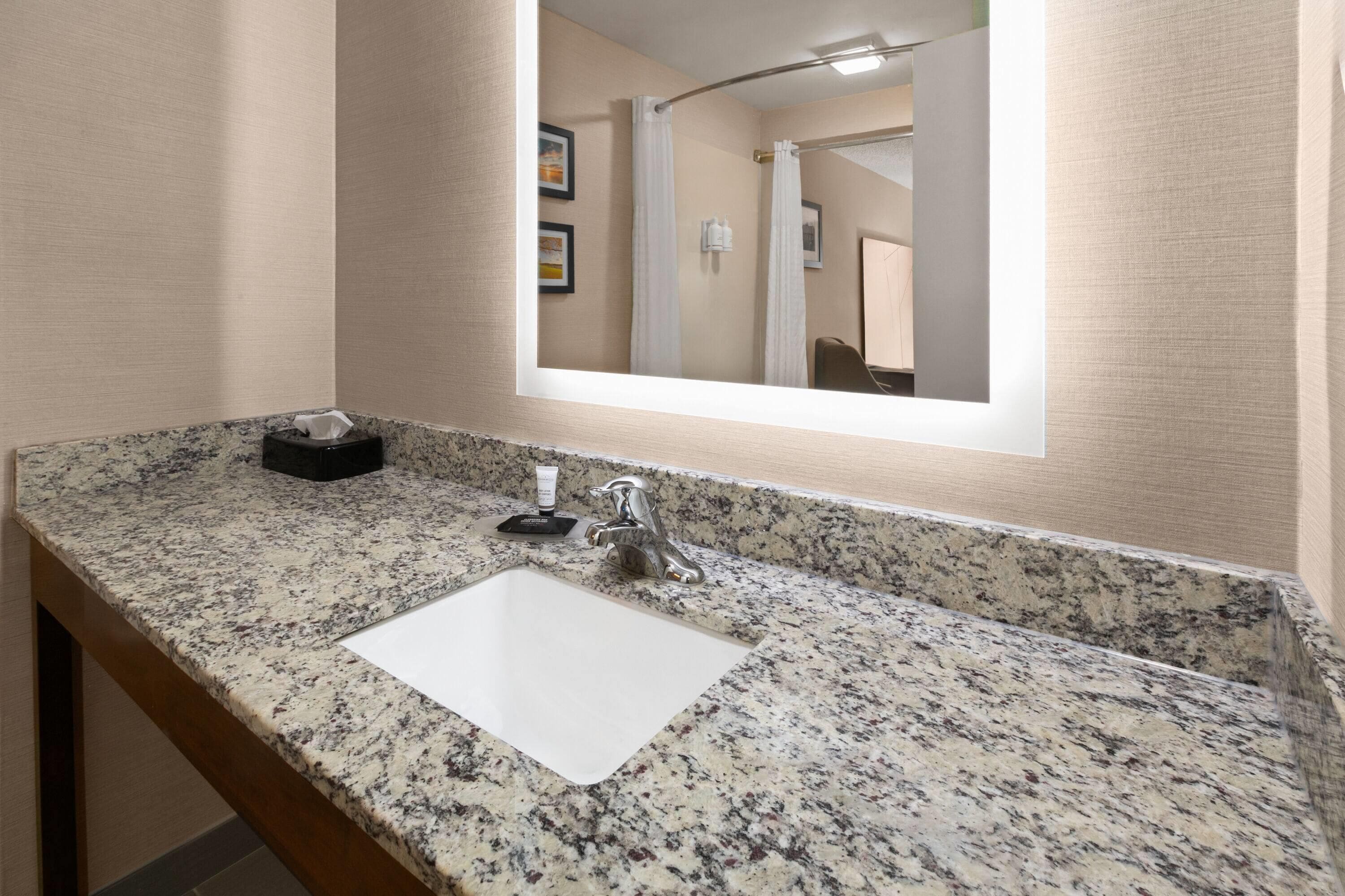 A bathroom with a granite countertop, a white sink, a mirror, and a towel rack.