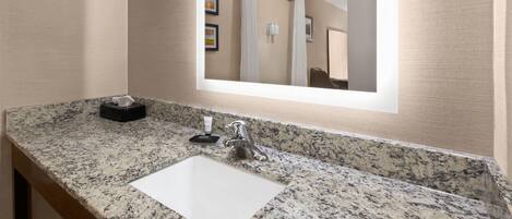 A bathroom with a granite countertop, a white sink, a mirror, and a towel rack.