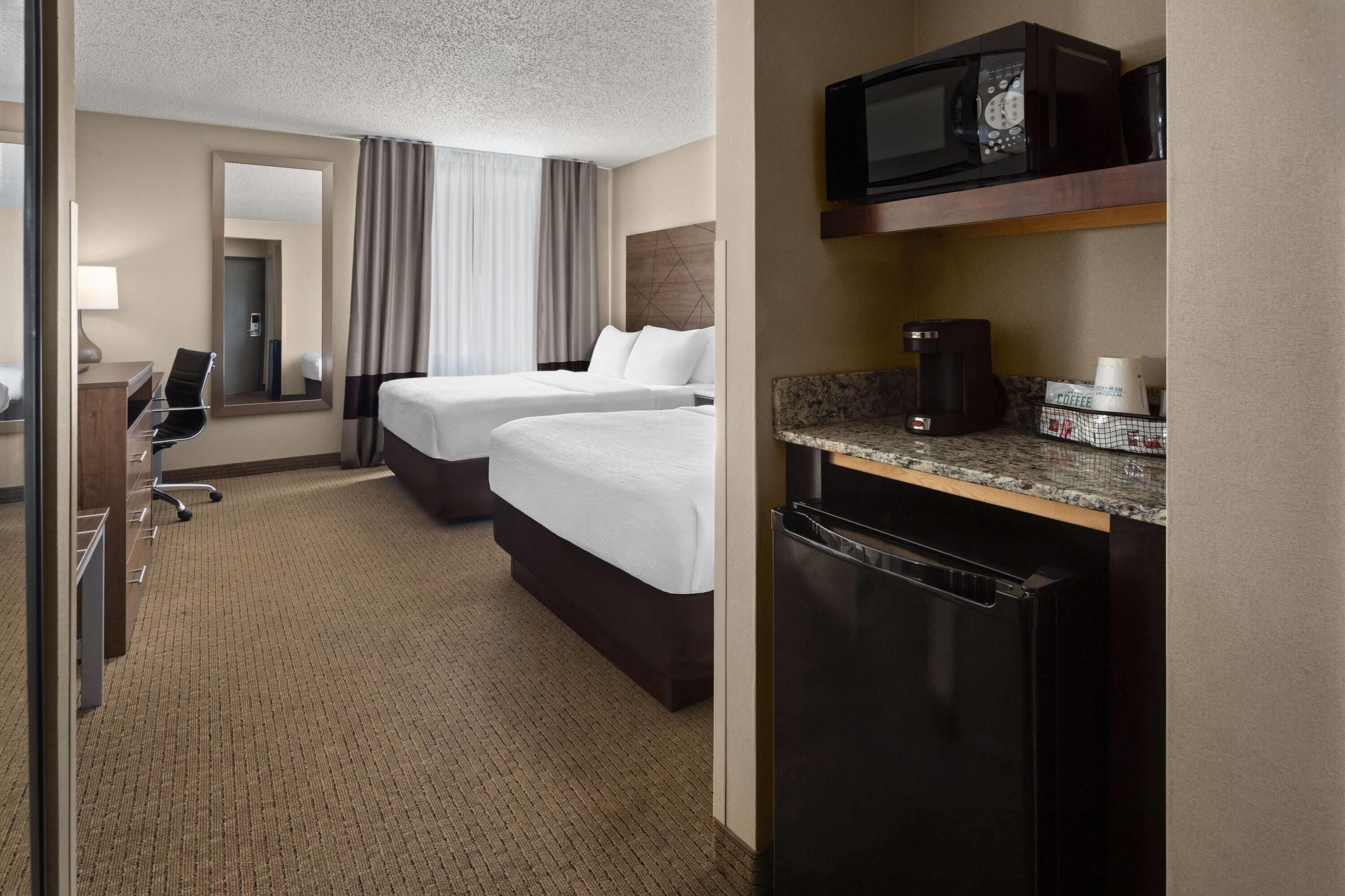 A hotel room with two beds, a desk, a chair, a microwave, a coffee maker, and a refrigerator.