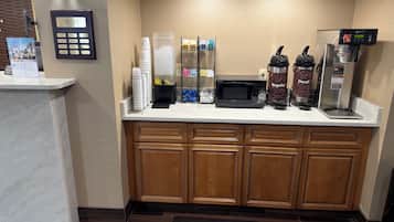A hotel reception area with a coffee machine, microwave, and a coffee dispenser.