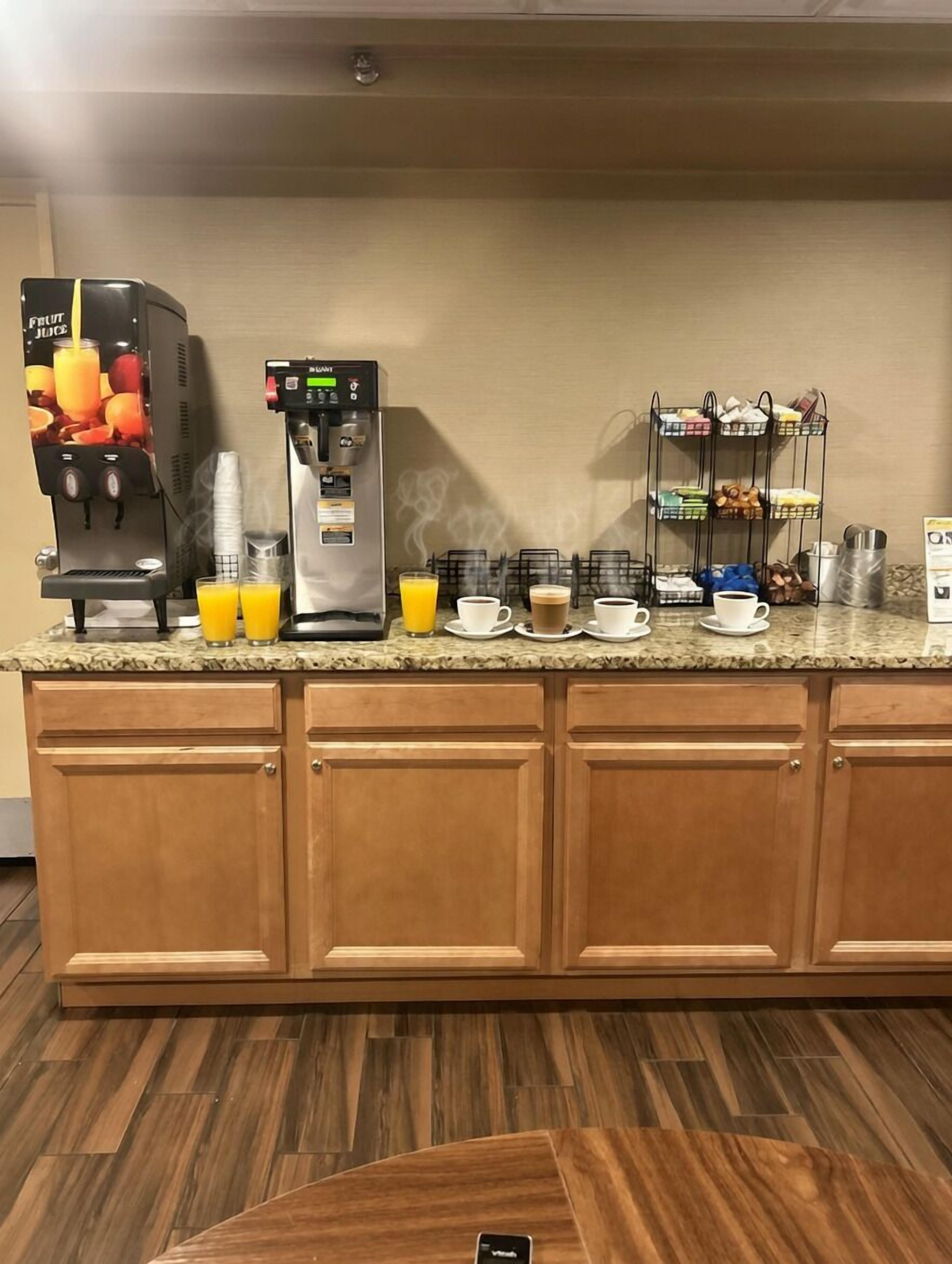 A hotel kitchen with a fruit juice dispenser, a coffee machine, and a buffet setup.