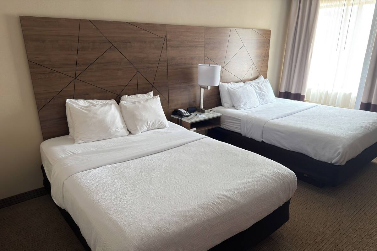 A hotel room with two beds, a wooden headboard, a bedside table with a lamp, and a phone.