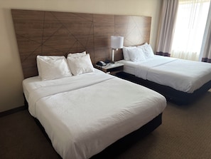 A hotel room with two beds, a wooden headboard, a bedside table with a lamp, and a phone.