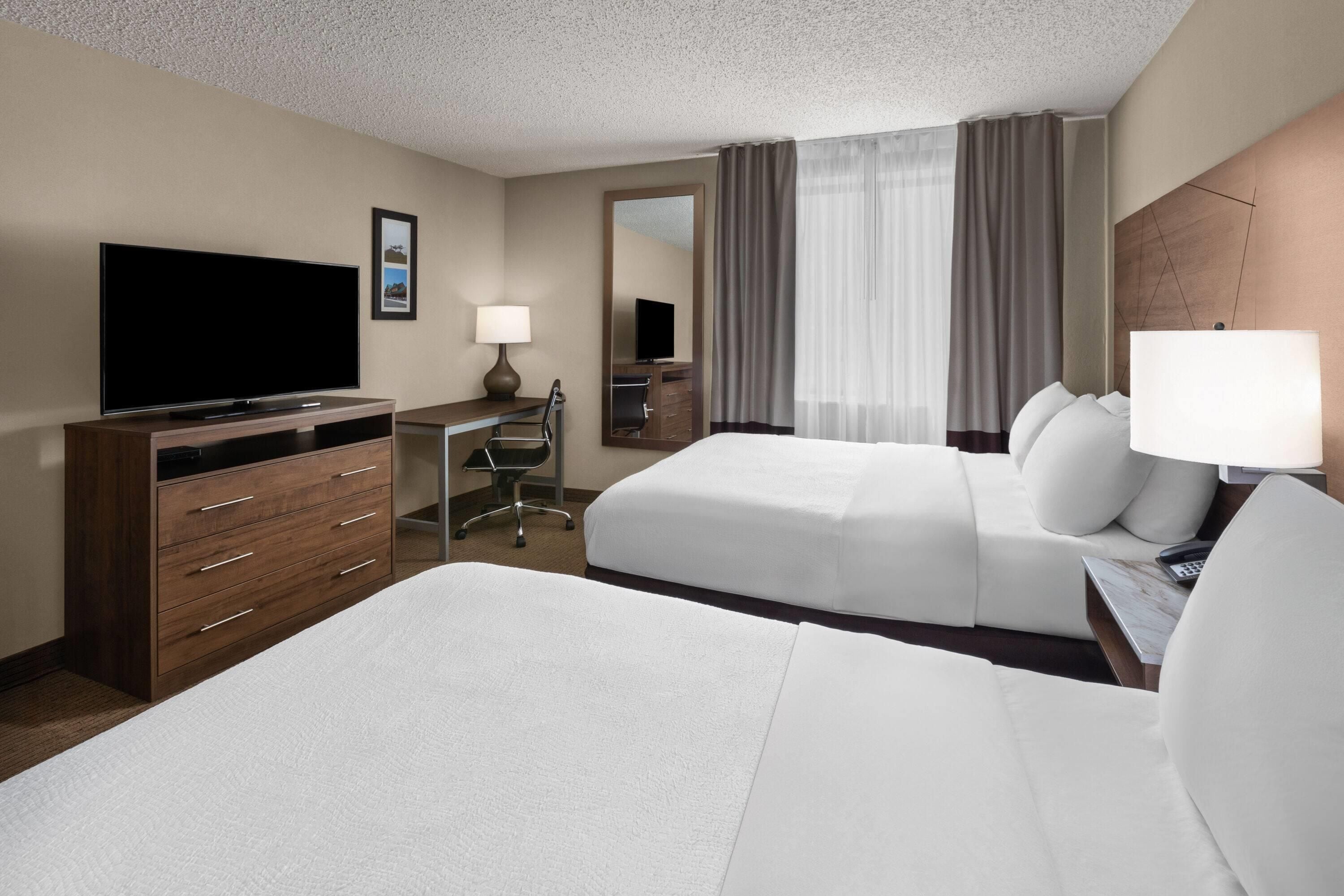 A hotel room with two beds, a desk, a television, and a mirror.