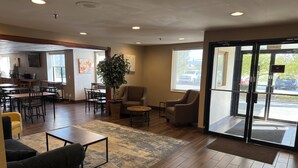 A spacious lobby with a wooden floor, a large potted plant, and a seating area with chairs and a sofa. - Wingate by Wyndham Utica (Utica)