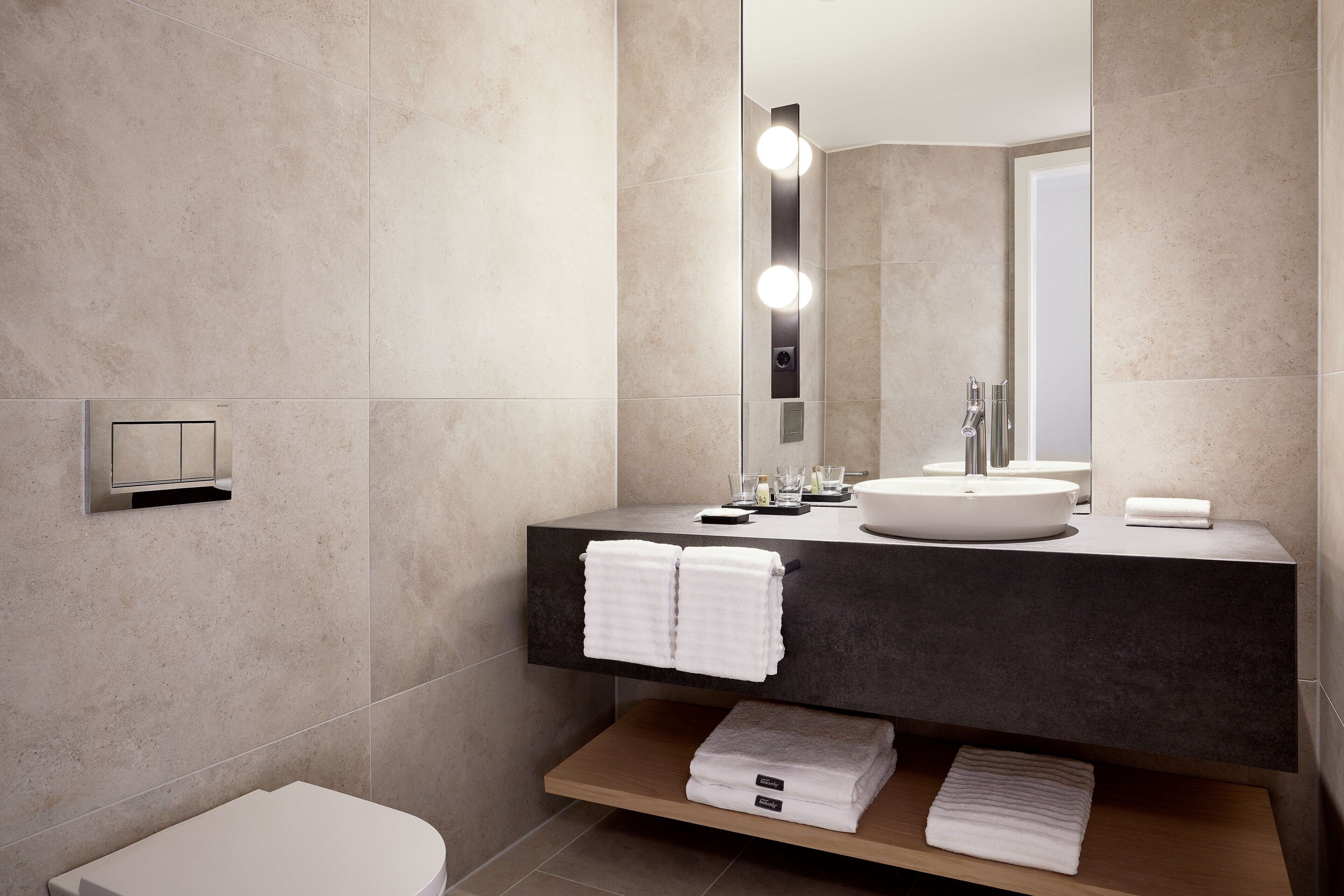 A modern bathroom with a large mirror, a round sink, and a toilet.