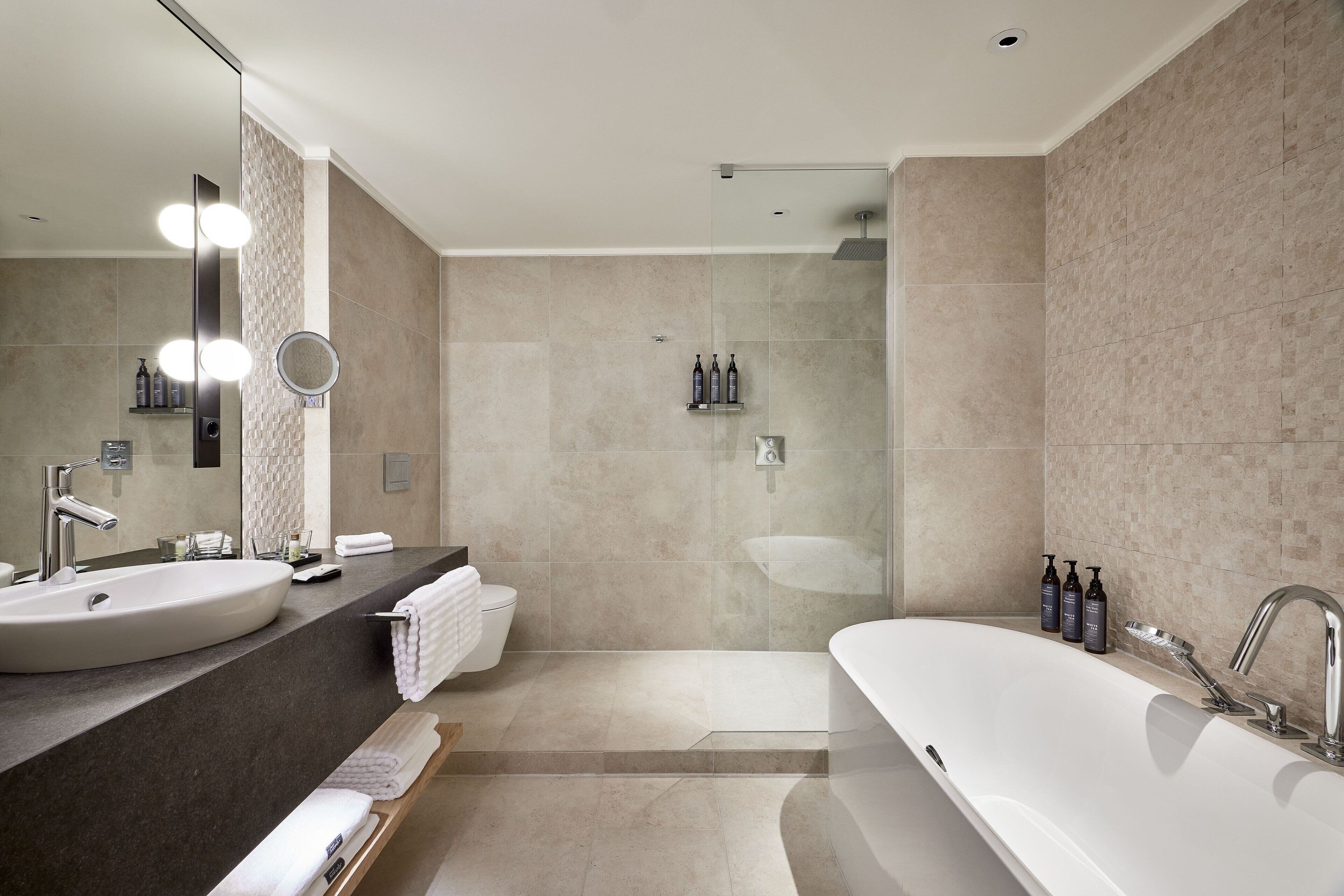 Ein modernes Badezimmer mit einer großen Badewanne, einem runden Spiegel und einer Duschkabine.