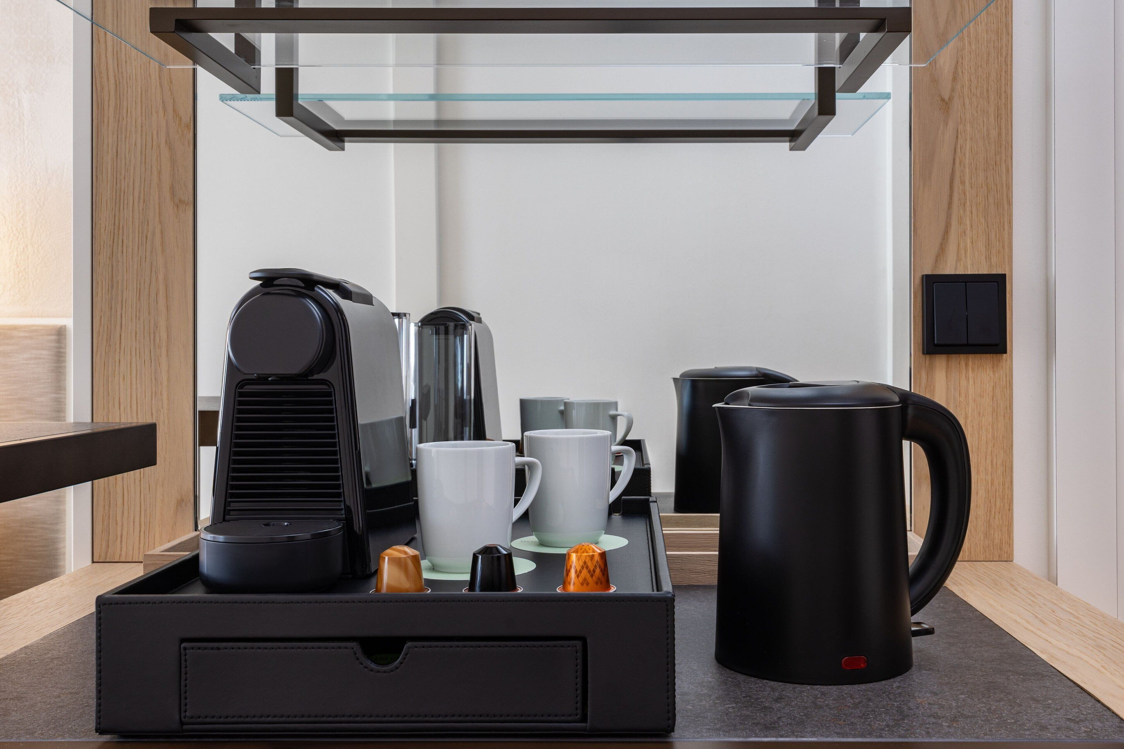 A modern kitchen area with a coffee station, including a coffee maker, cups, and a kettle.