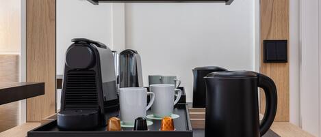 A modern kitchen area with a coffee station, including a coffee maker, cups, and a kettle.