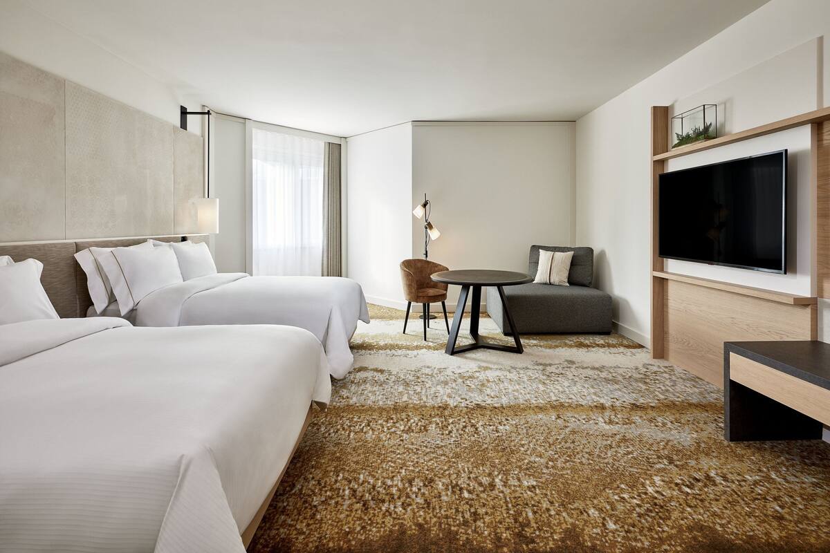 A hotel room with two beds, a sofa, a TV, and a small table.