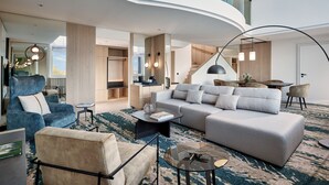 A modern living room with a curved ceiling, a grey sofa, a blue armchair, and a coffee table. - The Westin Grand Frankfurt (Frankfurt)