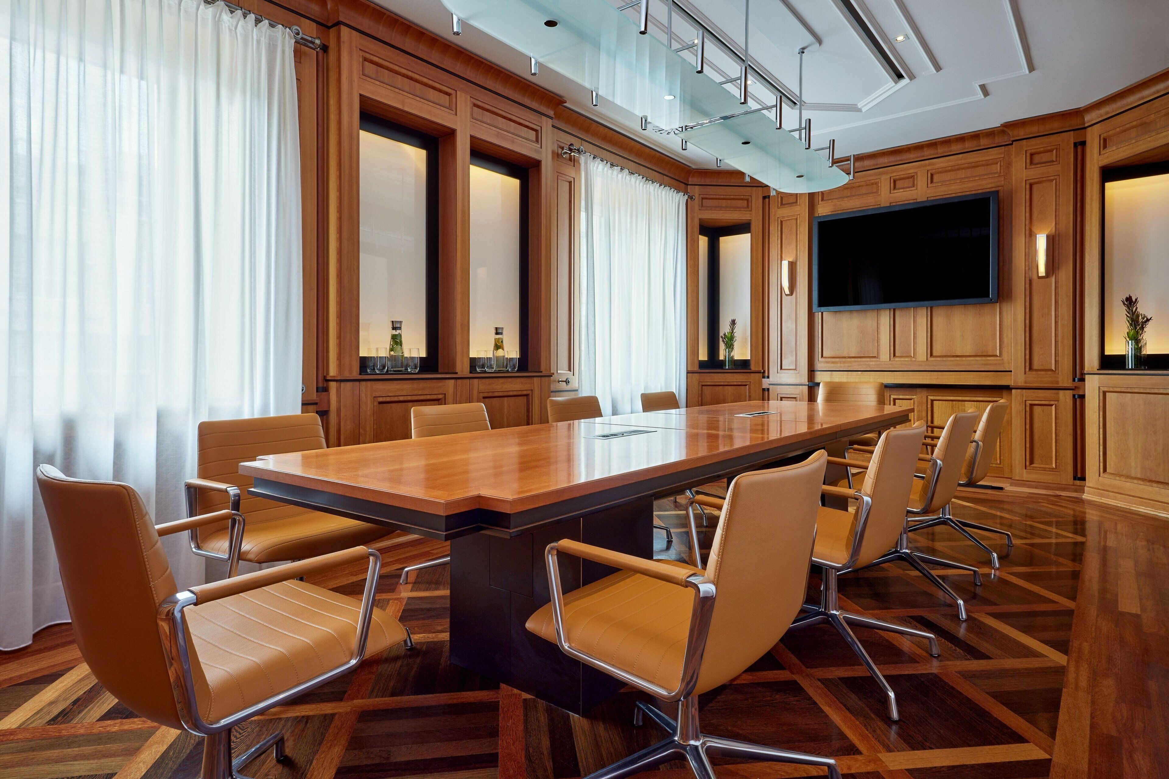 A conference room with a large wooden table, leather chairs, and a flat-screen TV.