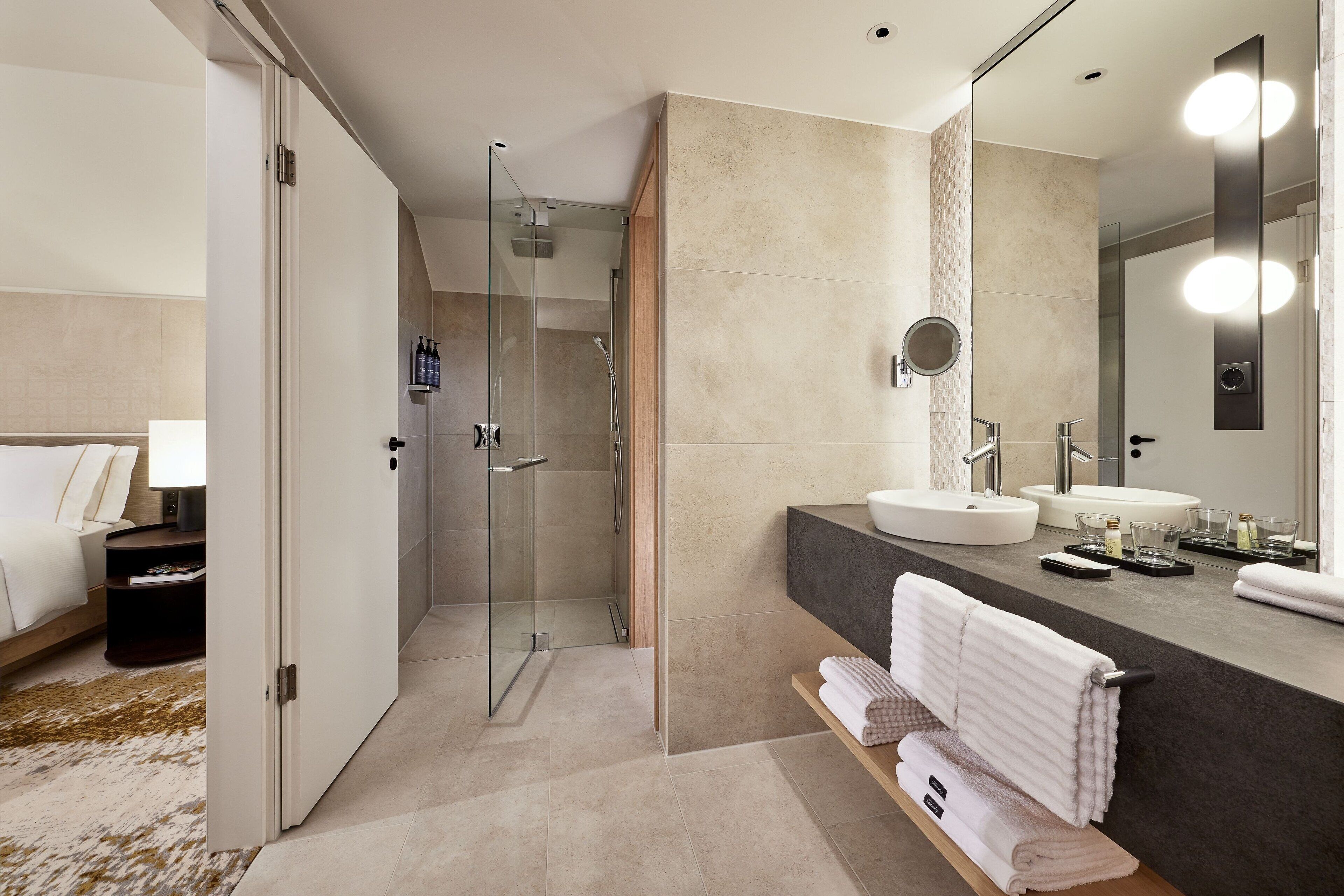 Een moderne badkamer met een douche met glazen wand, twee wasbakken en een grote spiegel.
