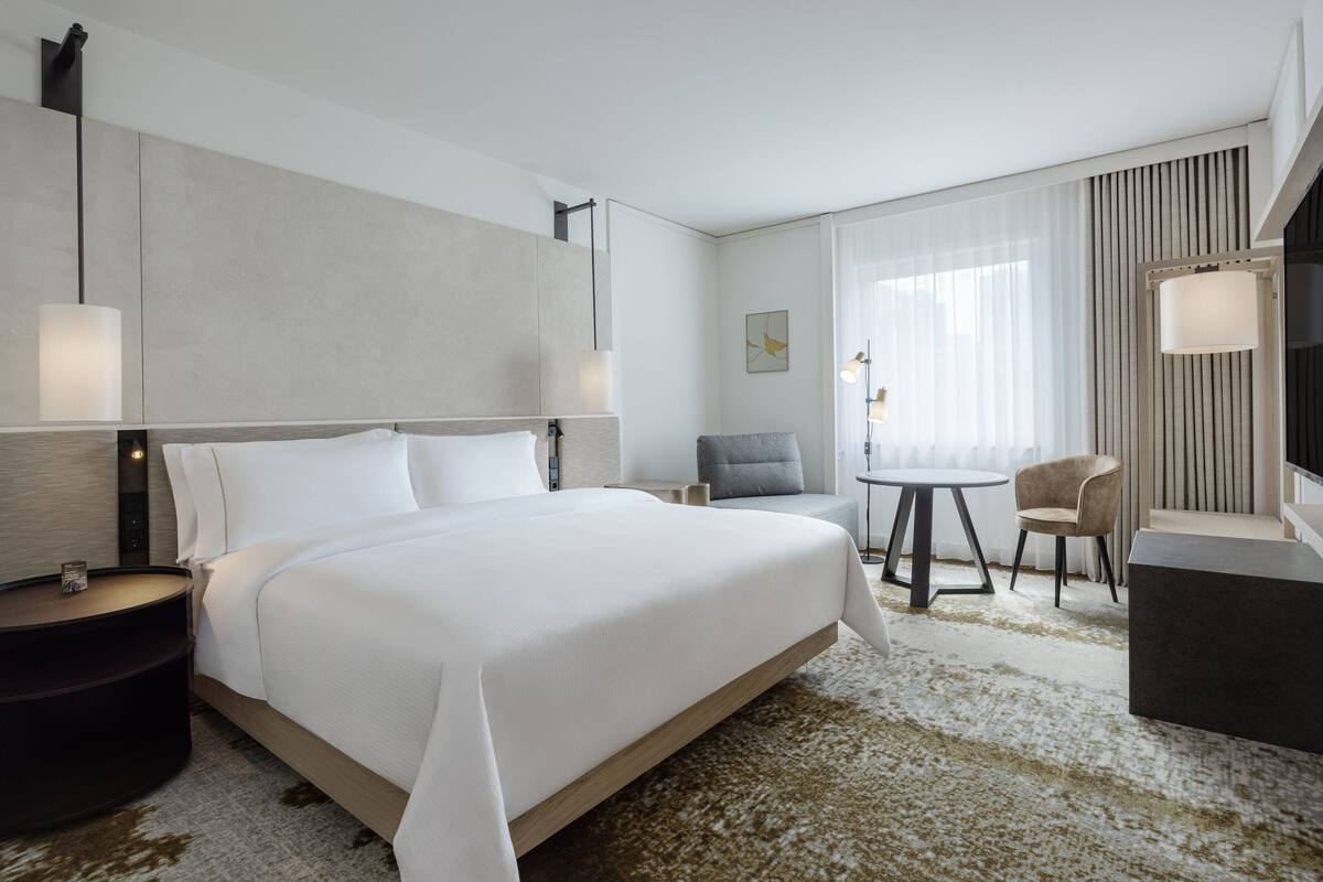 A modern hotel room with a large bed, a desk, a chair, and a TV.