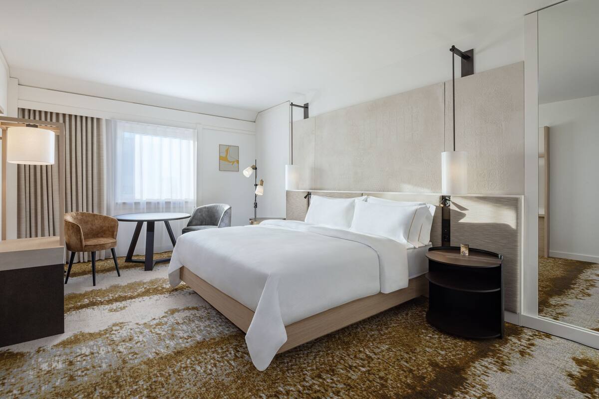 A hotel room with a large bed, a desk, a chair, a round table, and a large mirror.