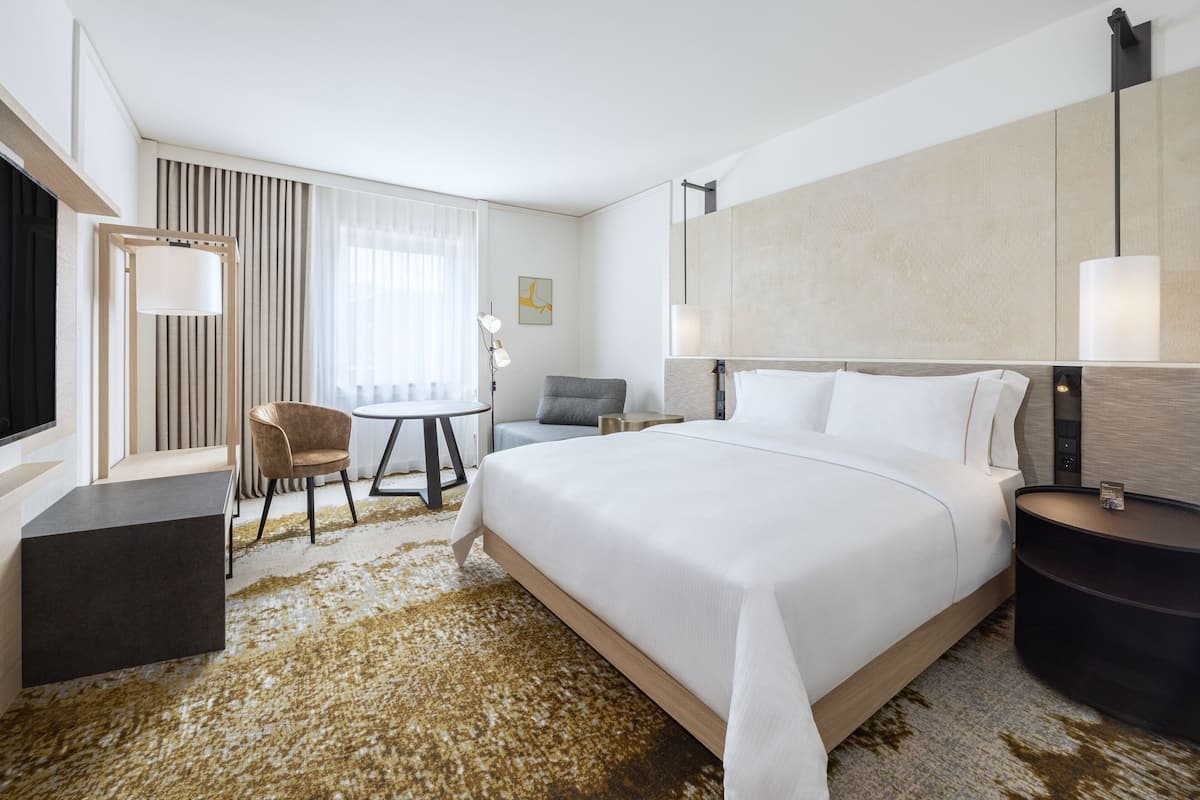 A modern hotel room with a large bed, a desk, a chair, and a small table.