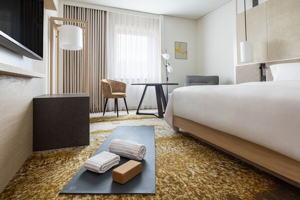 A hotel room with a bed, a desk, a chair, a yoga mat, and towels.