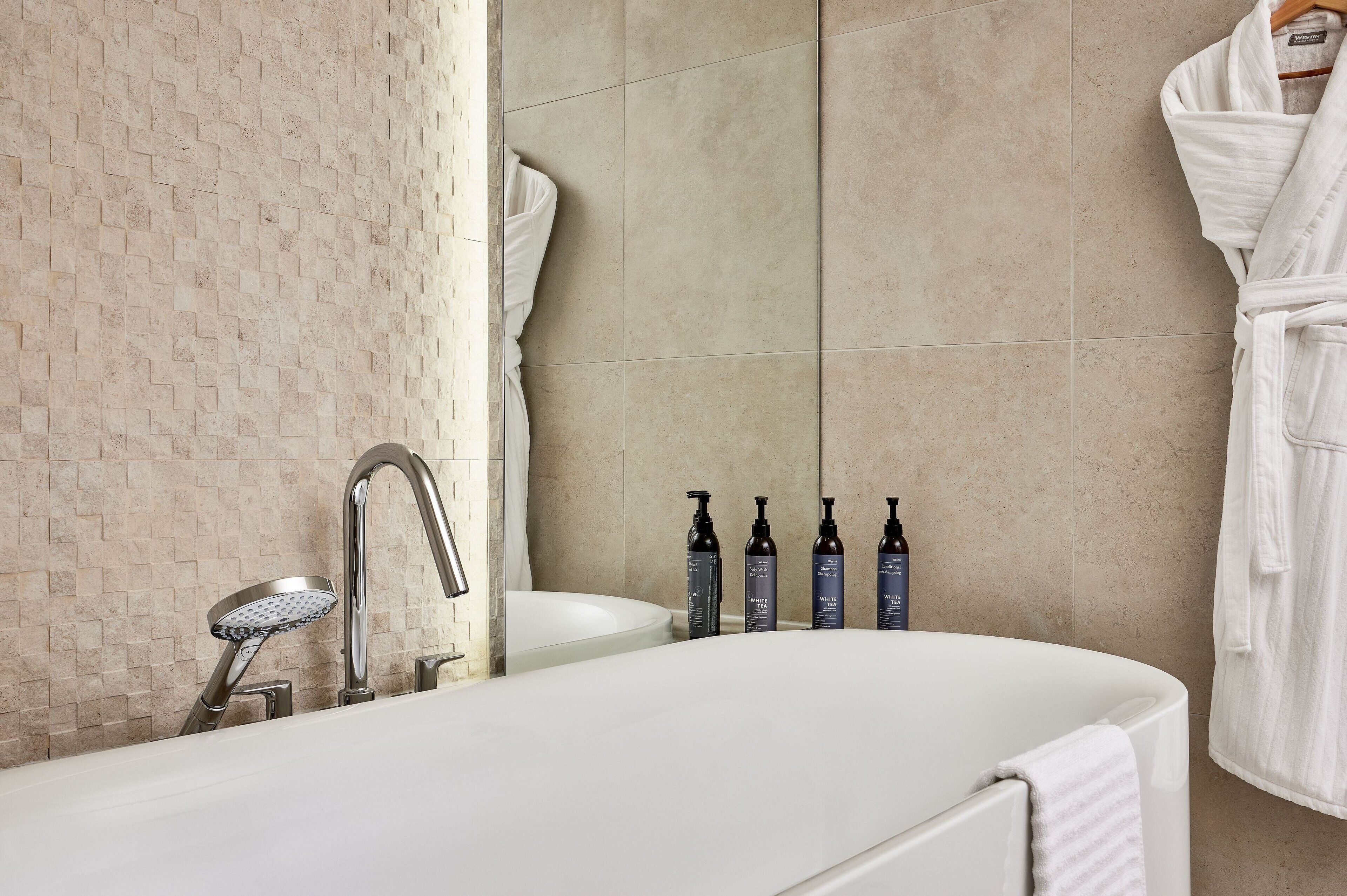 A modern bathroom with a white bathtub, a sink, and a shower. There are four bottles of toiletries on the wall.