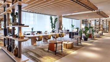 Eine geräumige, moderne Hotelhalle mit einer langen Rezeption, gemütlichen Sitzbereichen und einem großen Fenster, das für natürliches Licht sorgt.