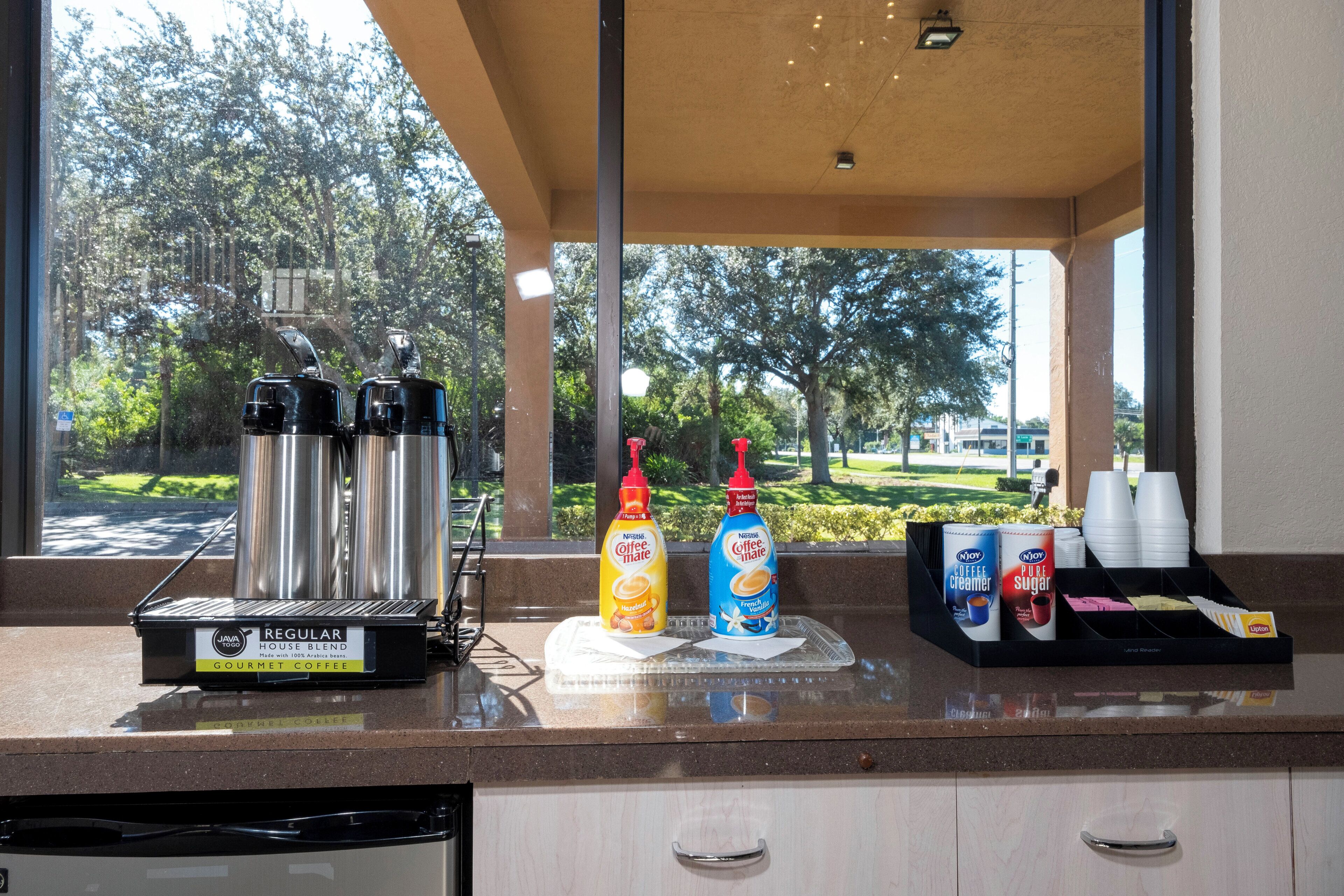 A coffee station with a coffee machine, two bottles of coffee creamer, and a box of creamer.