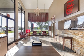 A hotel lobby with a reception desk, seating area, and a view of the outdoors. - Red Roof Inn Ft Pierce (Fort Pierce)