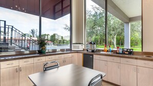 A modern kitchen with a dining table, cabinets, and a view of the street and trees outside.