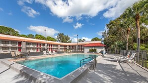 A hotel with a swimming pool, outdoor seating, and a red-roofed building.