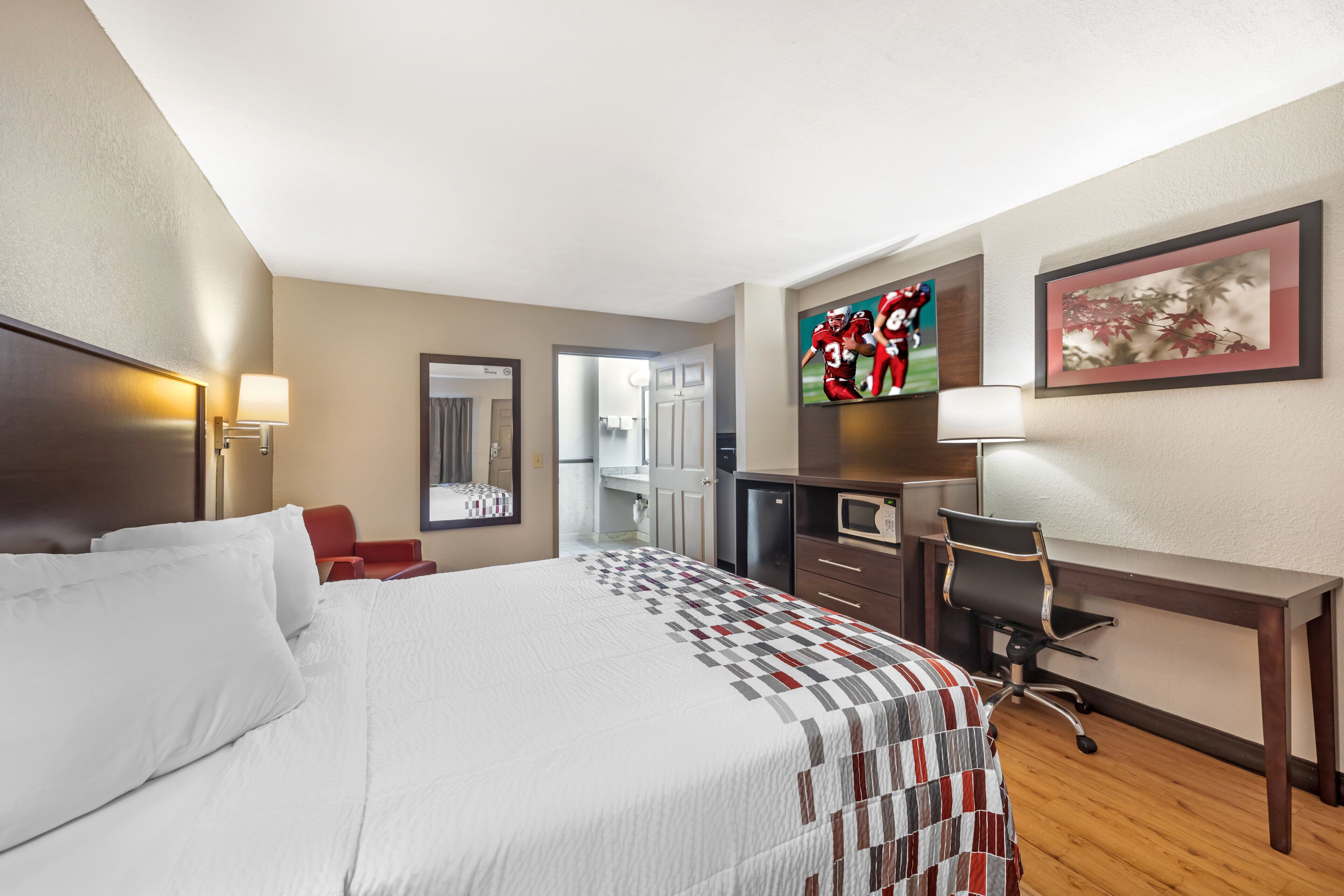 A hotel room with a large bed, a desk, a chair, a television, and a framed picture on the wall.