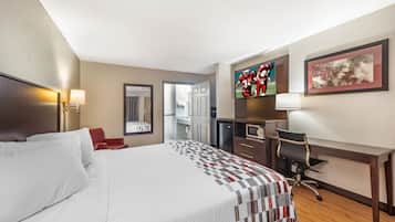 A hotel room with a large bed, a desk, a chair, a television, and a framed picture on the wall.