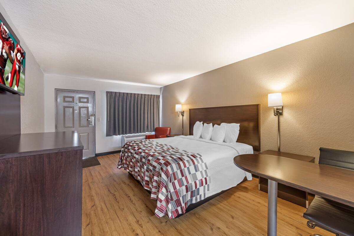 A hotel room with a large bed, a desk, a chair, a television, and a door.
