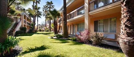 A hotel with a well-maintained lawn, palm trees, and a two-story building with balconies.
