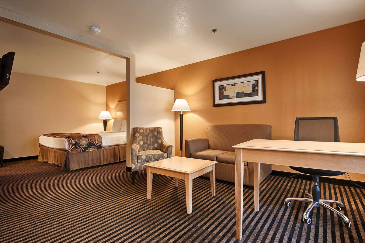 A hotel room with a bed, two chairs, a desk, a lamp, and a floor lamp.