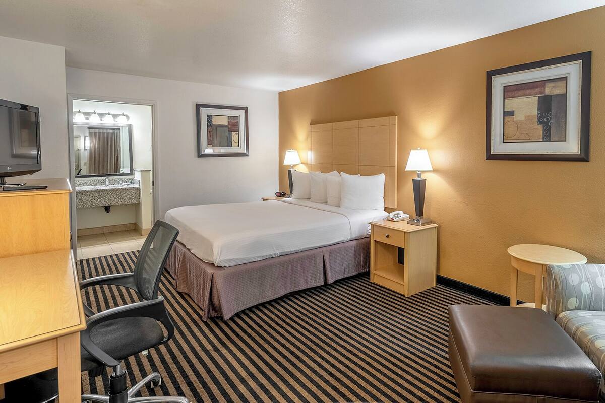A hotel room with a bed, desk, chair, and a small table.