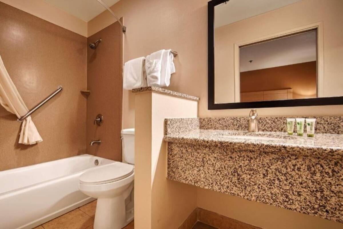 A bathroom with a bathtub, toilet, and a granite countertop with toiletries.