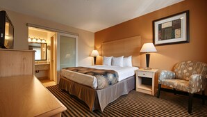 A hotel room with a bed, bedside lamps, a chair, a nightstand, and a mirror.