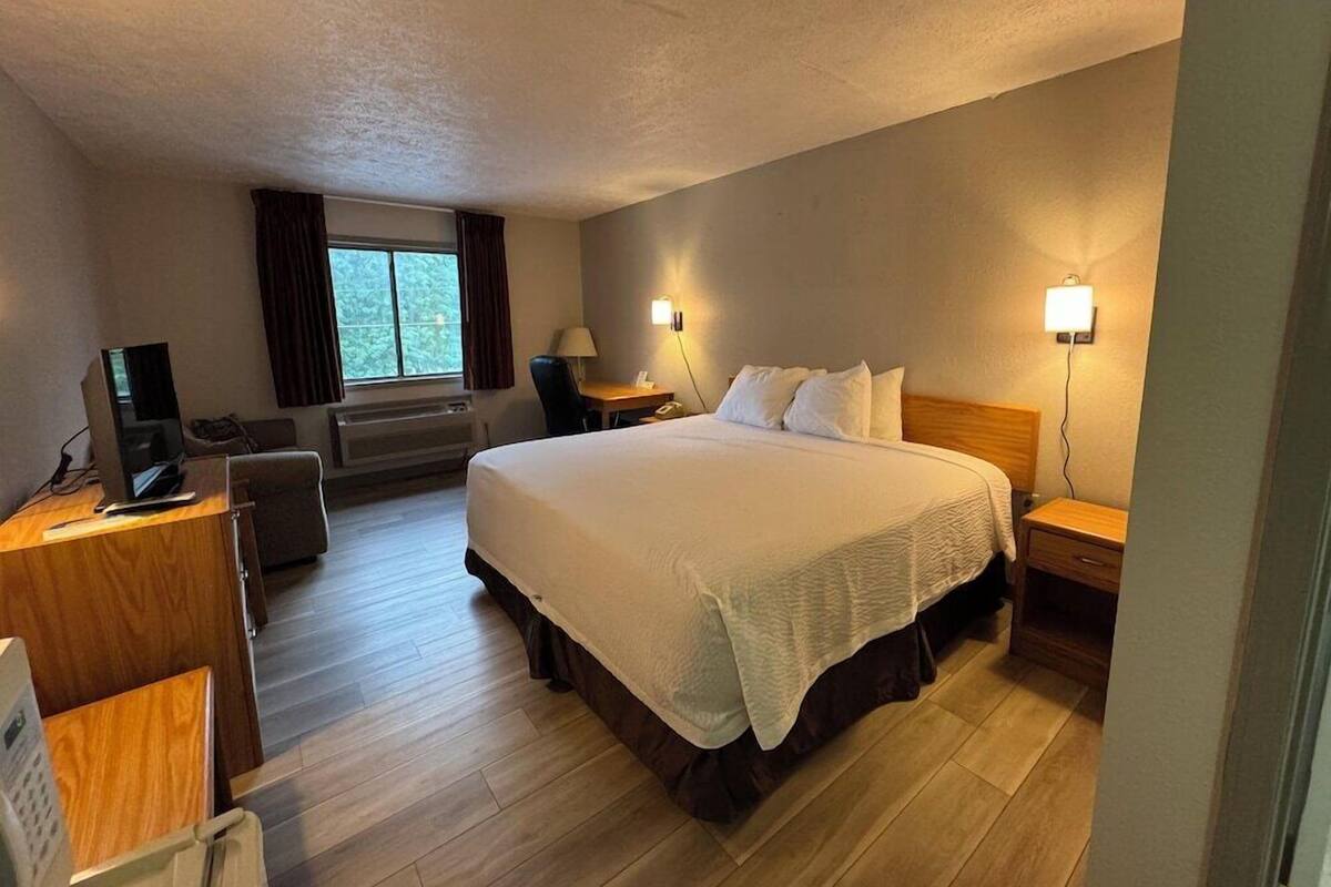 A hotel room with a large bed, a desk with a computer, a chair, a desk lamp, and a window with curtains.