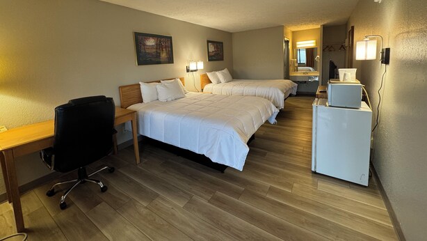 Ein Hotelzimmer mit zwei Betten, einem Schreibtisch, einem Sessel, einem kleinen Tisch und einer Mikrowelle.