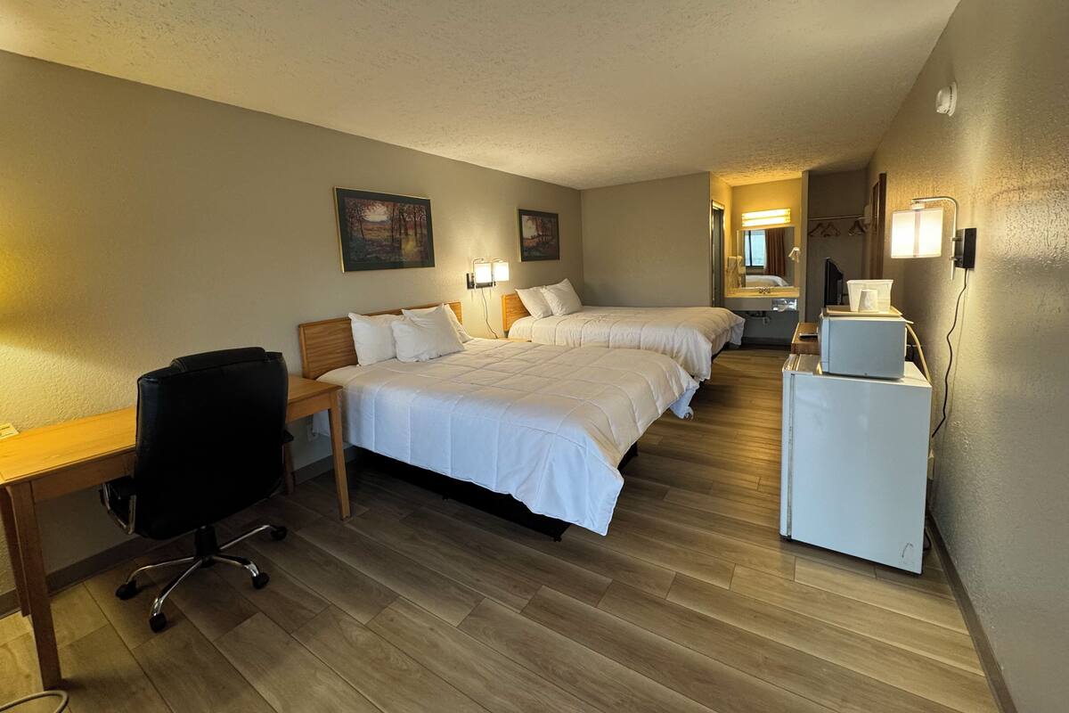 A hotel room with two beds, a desk, a chair, a small table, and a microwave.