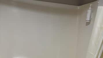 A bathtub with a white towel on the edge, a shower curtain, and a bottle of shampoo on the wall.