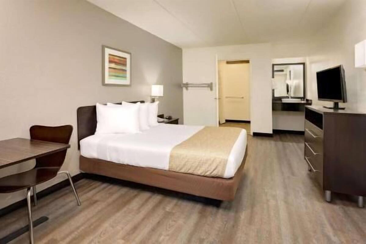 Ein Hotelzimmer mit Bett, Schreibtisch, Stuhl, Fernseher und einer Küchenzeile.