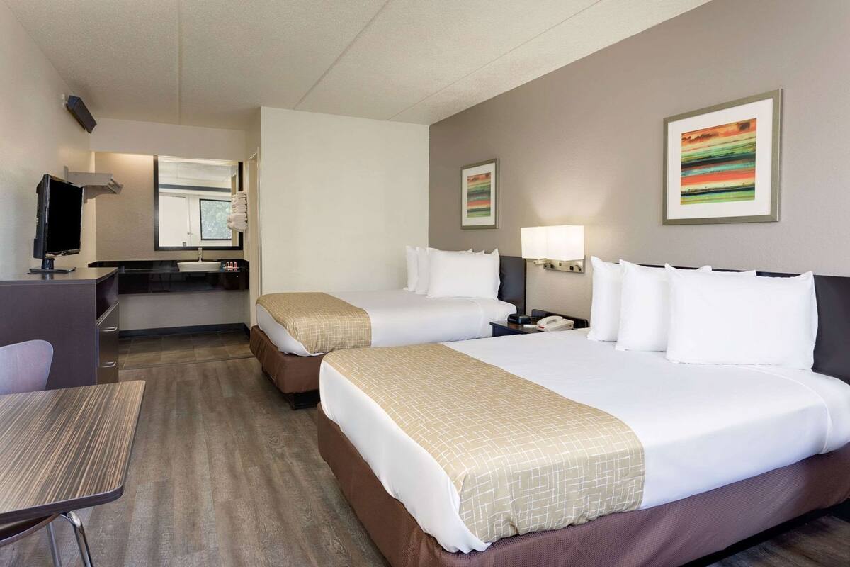 Ein Hotelzimmer mit zwei Betten, einem Schreibtisch, einem Stuhl, einem Fernseher und Bildern an den Wänden.