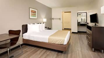 A hotel room with a bed, desk, chair, TV, and a bathroom visible through an open door.
