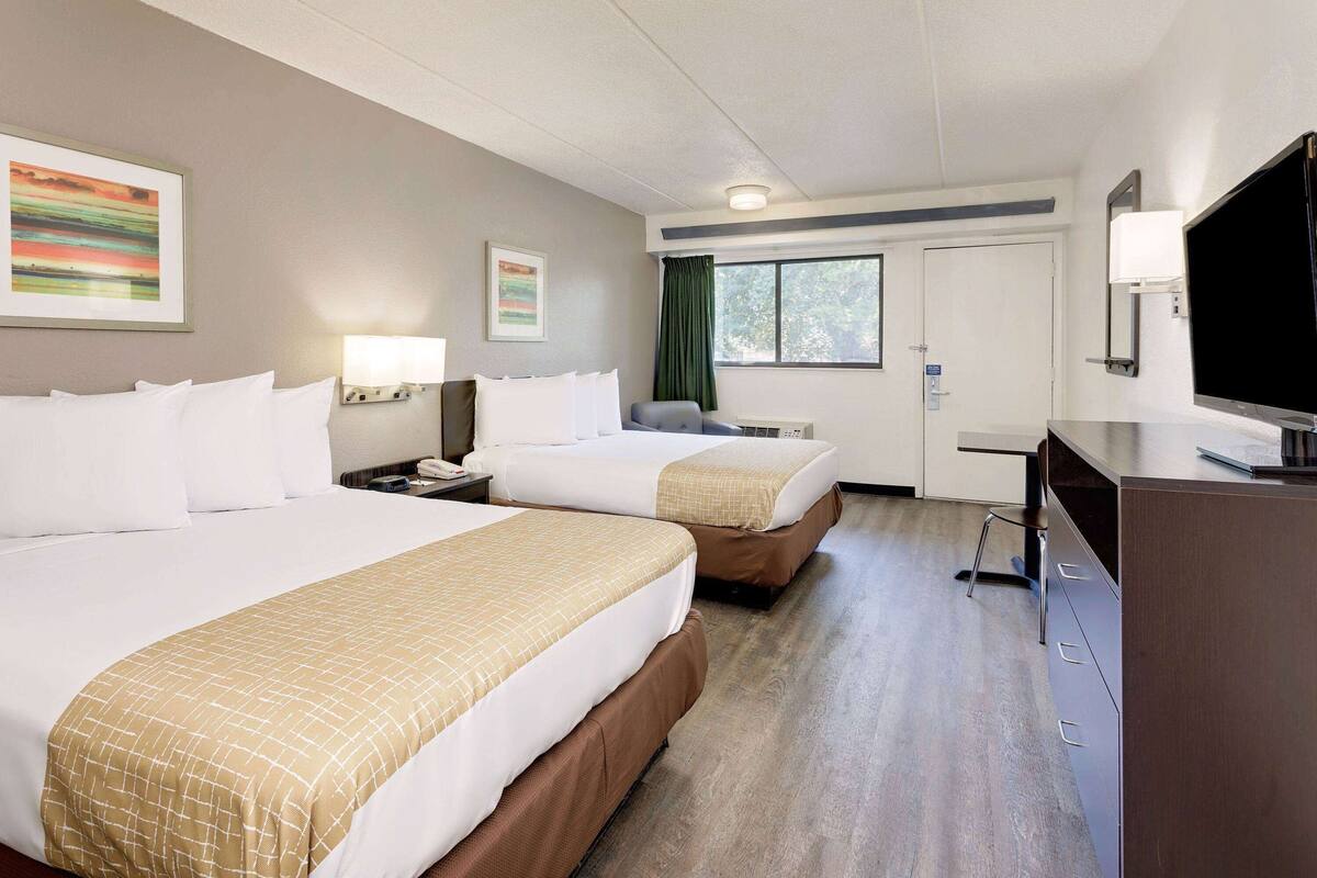 Ein Hotelzimmer mit zwei Betten, einem Schreibtisch, einem Fernseher und einem Fenster mit Vorhängen.