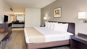 Une chambre d’hôtel avec un grand lit, un bureau, une chaise, une télévision et une salle de bain visible au fond.