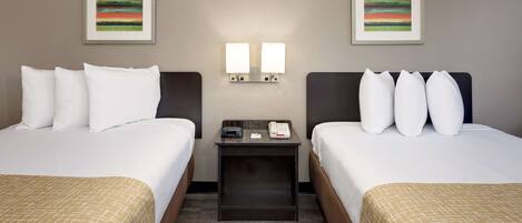 Una habitación de hotel con dos camas, una mesita de noche con un teléfono y un reloj, y dos luces fijadas en la pared.