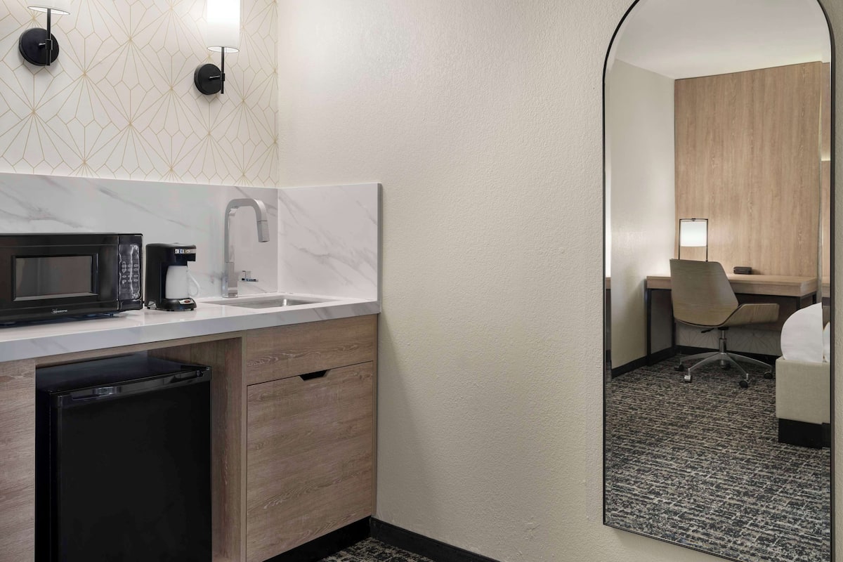 A modern hotel bathroom with a sink, a microwave, a coffee maker, and a mirror.