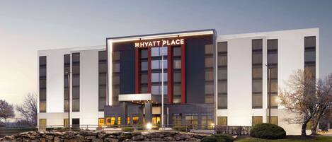 Un moderno hotel Hyatt Place con una entrada destacada, ventanas amplias y un muro de contención de piedra en primer plano.