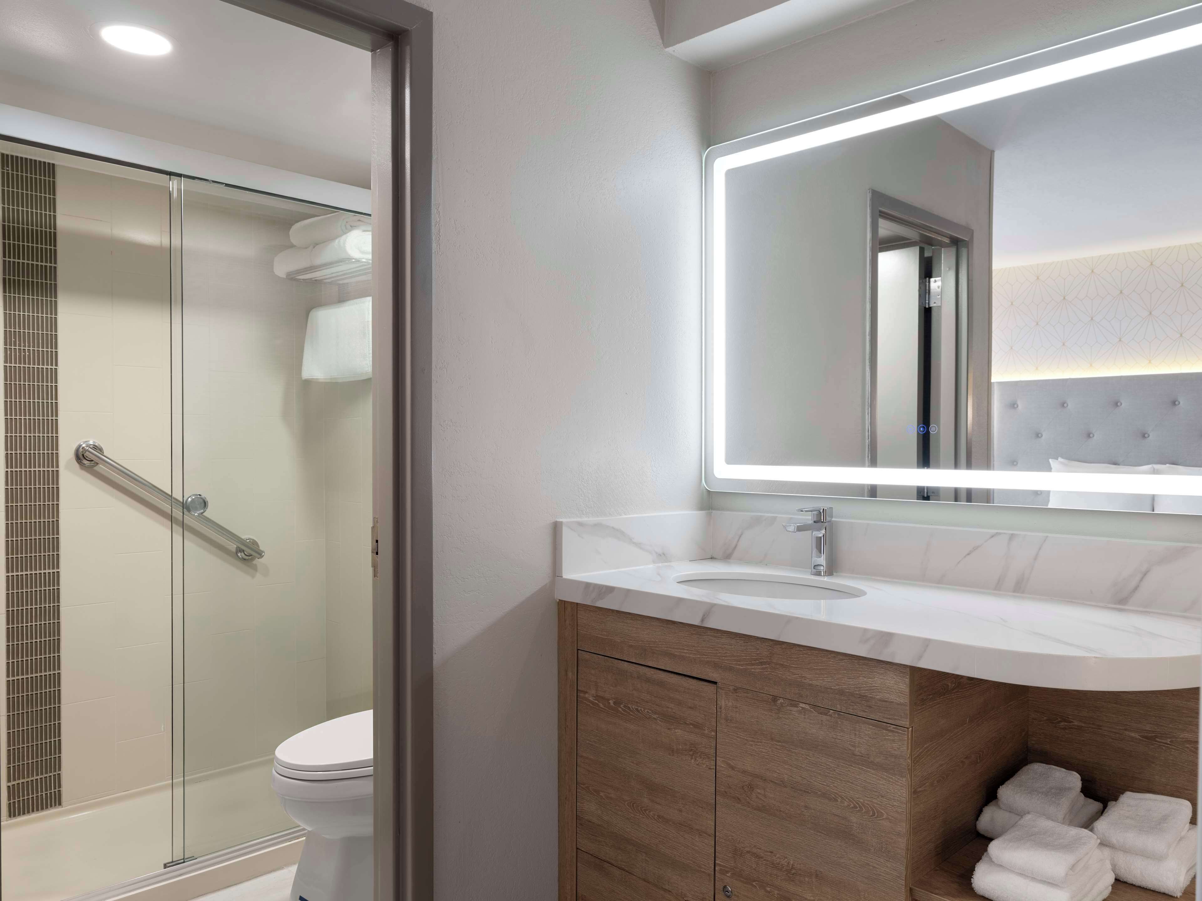 A modern bathroom with a glass shower enclosure, a white toilet, a vanity with a marble countertop, and a mirror with integrated lighting.